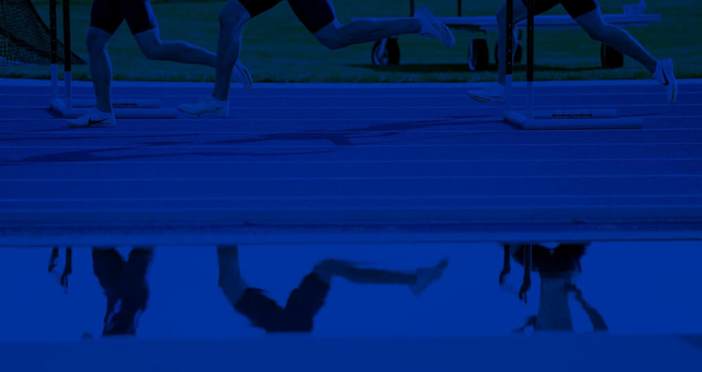 An artistic crop of three runners legs on a blue track, a reflection of their legs at the bottom from a pool of water